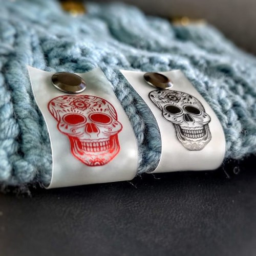 Silikonowa metka z czarnym nadrukiem czaszki Calavera na mlecznym, półprzezroczystym tle.