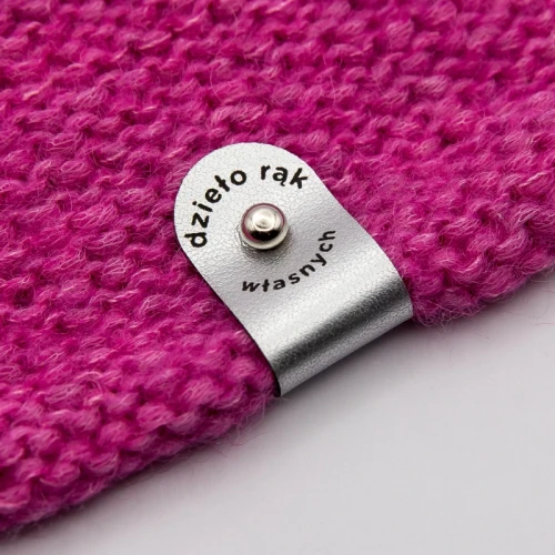 Srebrna metka z grawerem „Dzieło rąk własnych” na różowym swetrze.