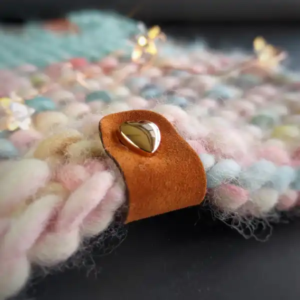 Brązowa metka z Alcantary ze złotym nitem w kształcie serca na kolorowym, wzorzystym kocyku handmade