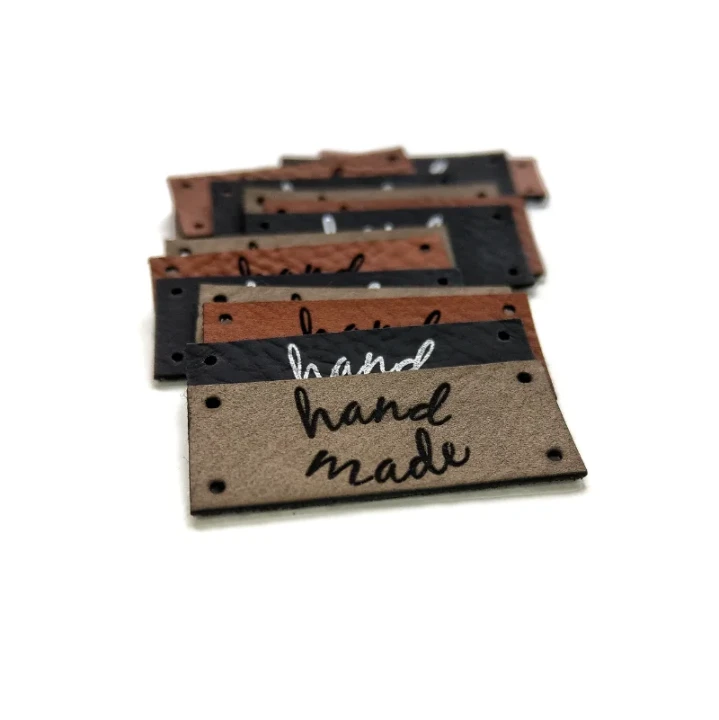 Zbliżenie na dwurzędowy układ napisu hand made na jasnoszarej naszywce o wymiarach 35x15 mm.webp